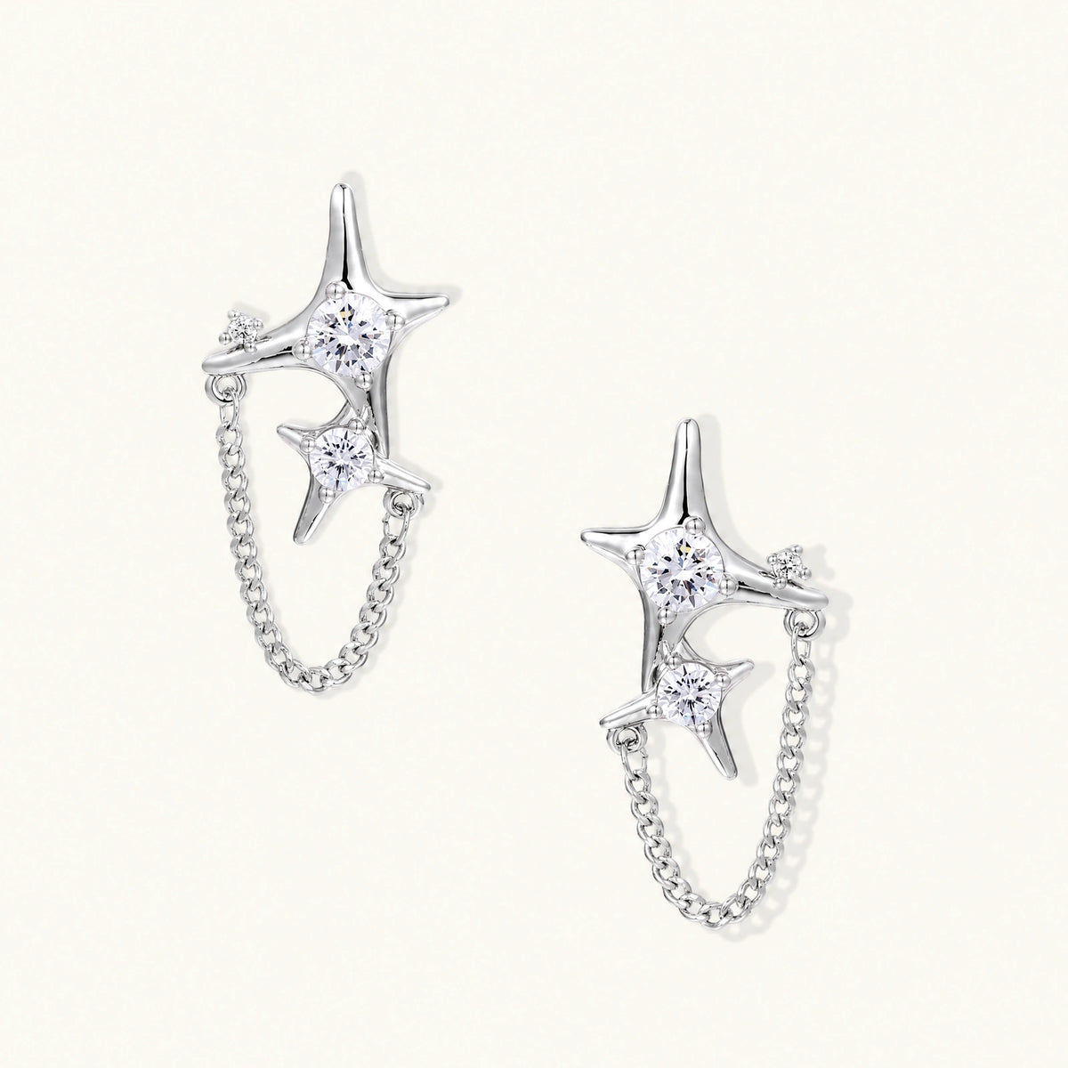 Silver star studs with crescent moon cutouts and zirconia stones connected by delicate chains on white background