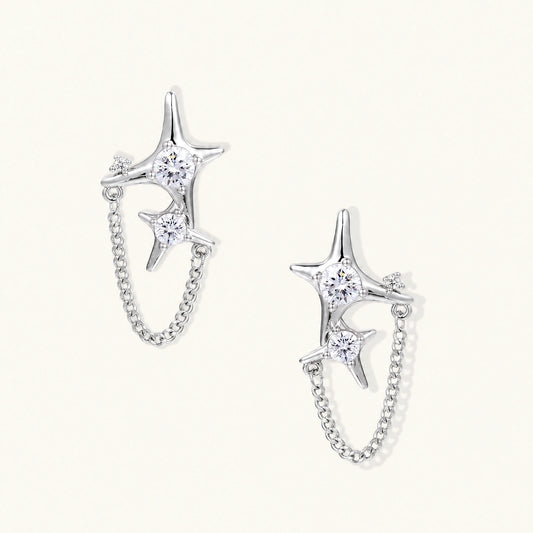 Silver star studs with crescent moon cutouts and zirconia stones connected by delicate chains on white background