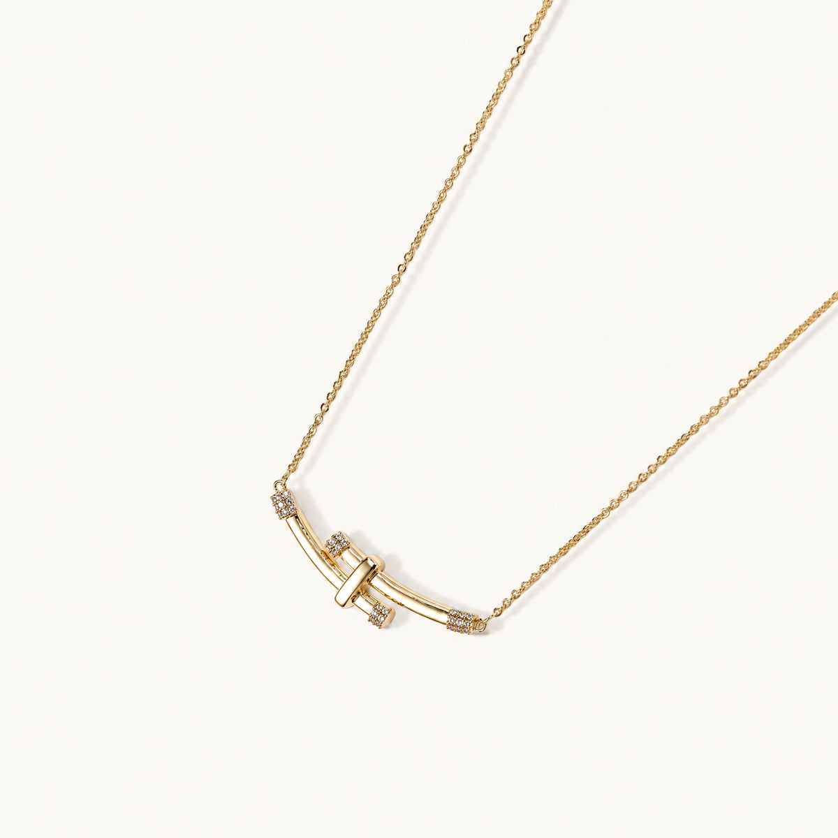 Gold-plated curved bar necklace with diamond accents on delicate chain against cream background