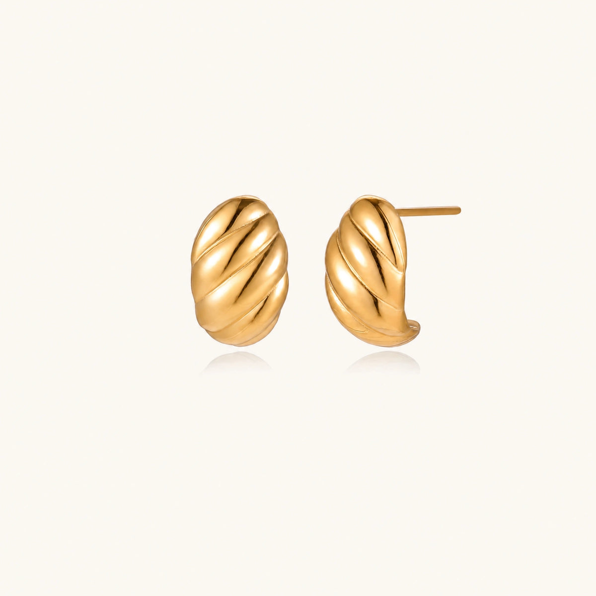 Chunky gold twisted rope huggie hoops with diagonal grooves and high-polish finish on cream background